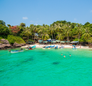 Kleine tropische Bucht in Vietnam mit Booten im klaren grünen Wasser, umgeben von Palmen und dichter Vegetation.