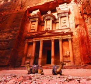 Zwei Kamele ruhen vor der in Felsen gehauenen Fassade des Schatzhauses von Petra in Jordanien.