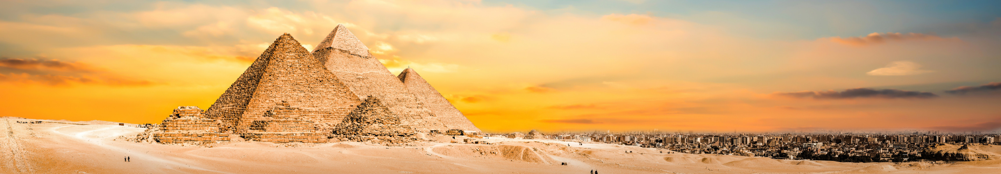 Die Pyramiden von Gizeh in &Auml;gypten bei Sonnenuntergang mit goldfarbenem Himmel und Kamelen in der W&uuml;ste