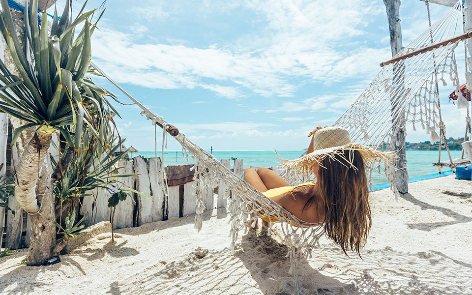 Fr&uuml;hbucher Urlaub: Frau liegt in H&auml;ngematte am Strand mit Meerblick