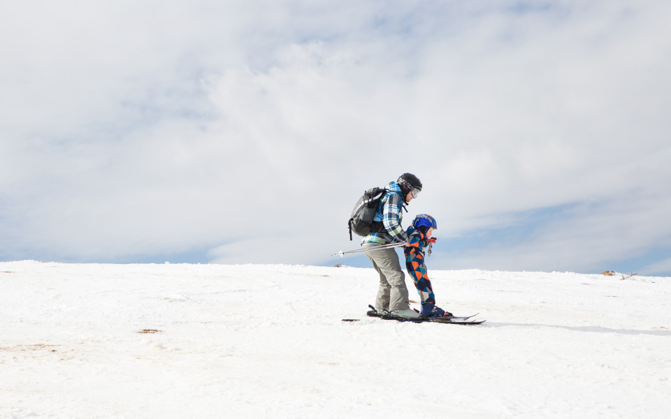 Kind und ein Erwachsener in warmen Overalls, die Skifahren &uuml;ben. 
