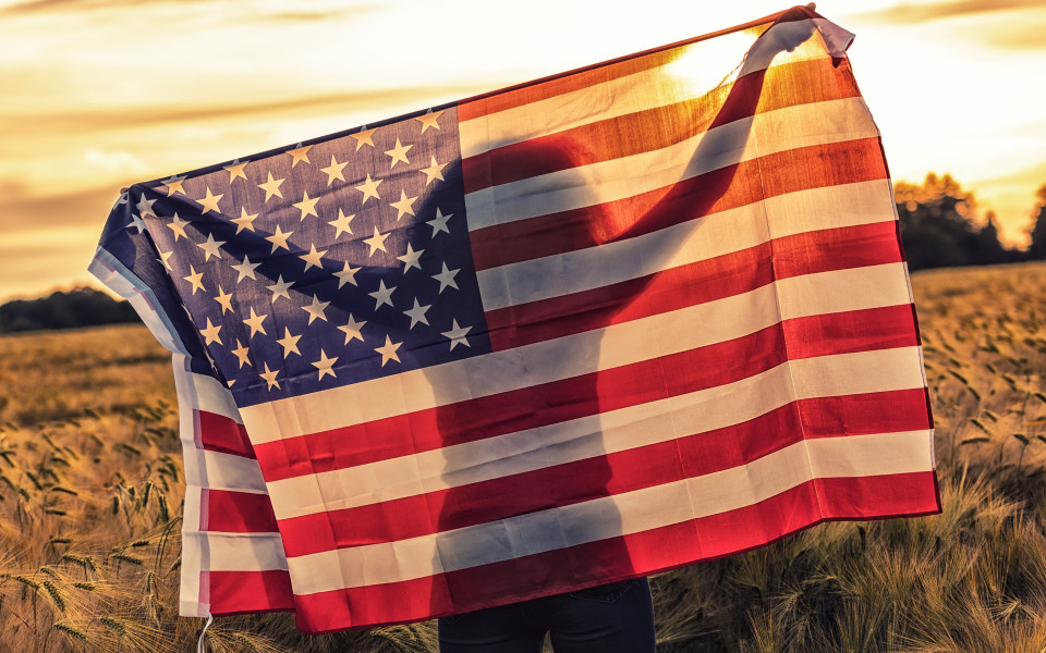 Silhouette einer jungen Frau mit USA-Flagge im Feld bei Sonnenuntergang