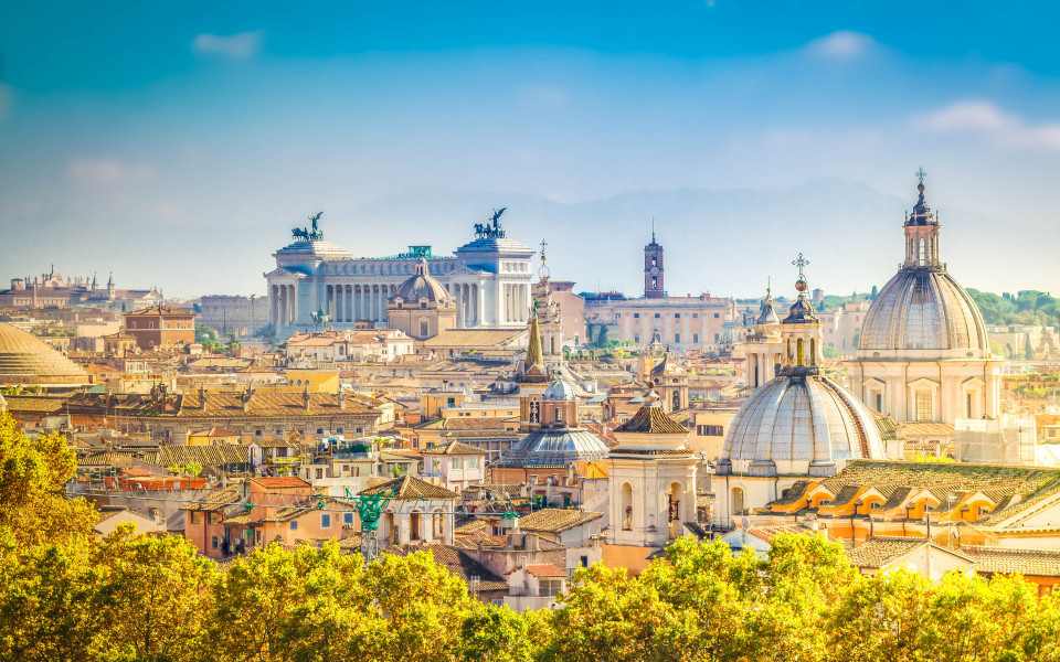 Blick &uuml;ber die D&auml;cher von Rom mit charakteristischen Kuppeln und dem Monumento a Vittorio Emanuele II im Hintergrund.