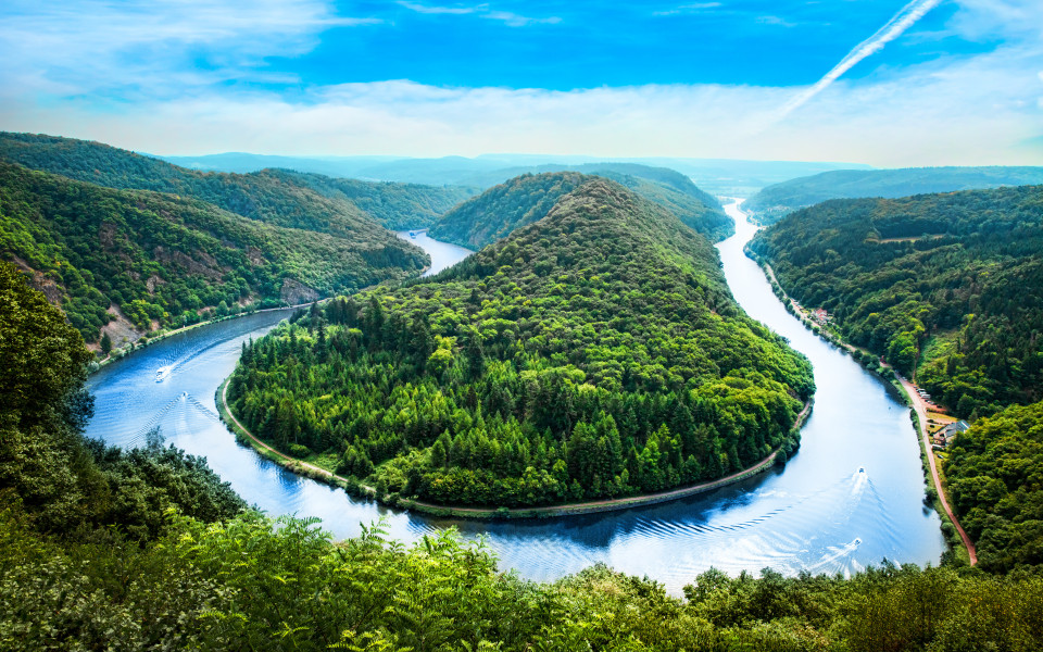 Die Saar in einer Schleife, umgeben von &uuml;ppigem Gr&uuml;n und sanften H&uuml;geln, mit einem Boot auf dem Fluss.