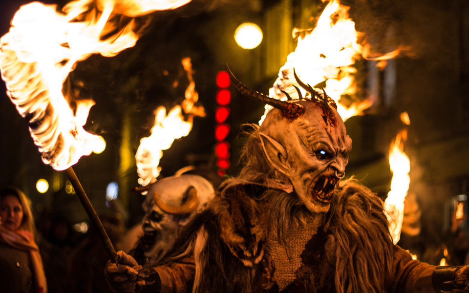 Krampus mit furchteinfl&ouml;&szlig;ender Maske und Fackel beim traditionellen Krampuslauf in den Alpen.